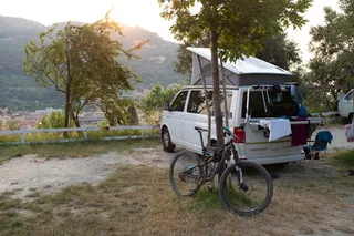 Camping holiday by bike: a camper stands on a campsite with great views from above to a city, while laundry on the bicycle carrier is dries and a bicycle is stretched on the tree