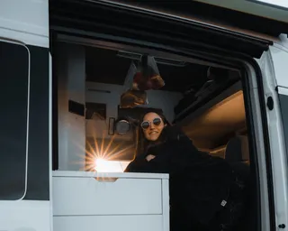 Frau mit Sonnenbrille schaut bei Sonnenuntergang aus ihrem Camper in Holland