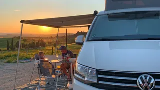 Vater sitzt mit seinem Sohn vor einem Camper in der Toskana und genießt den Sonnenuntergang.