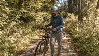 A young man with a helmet and a sports jacket on his bike holiday in Germany pushes his mountain bike on a forest path