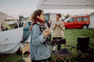 Eine Frau steht mit einem Tischtennisball auf einem Festivalgelände, um sie herum sieht man Zelte, Campingstühle und eine weitere Frau im Hintergrund. Unsere Festival Packliste findest du hier.