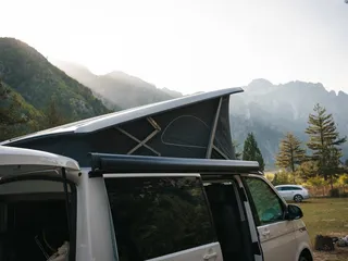 Campsites Dolomites: A camper with open roof stands in front of a mountain scenery in the sun